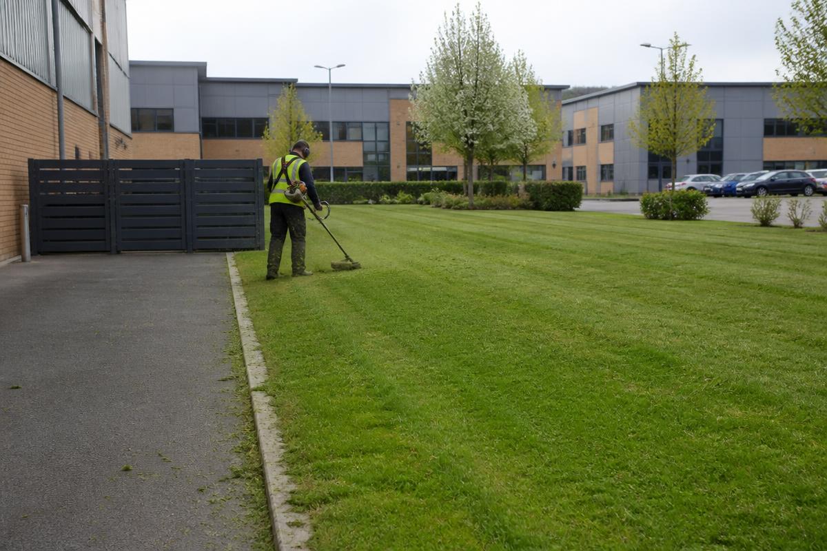 Grounds maintenance worker strimming a communal lawn at a commercial business park