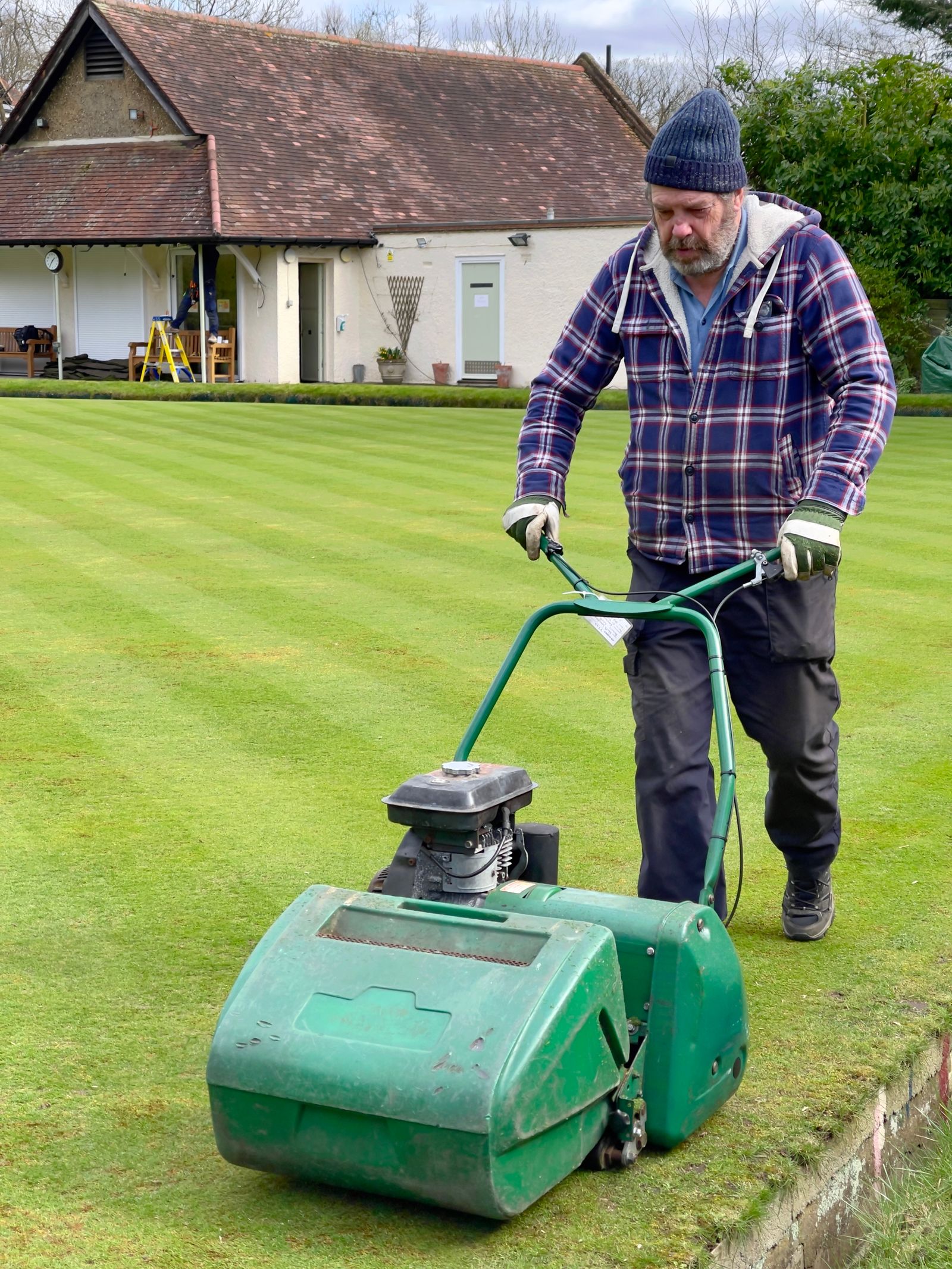 Gardener mowing a striped lawn outside a home in Wokingham