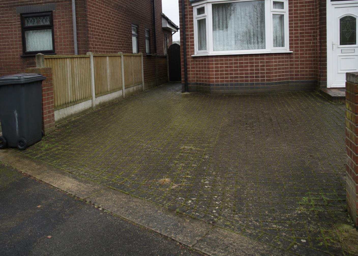 Block-paved driveway covered in green algae and moss before jet washing